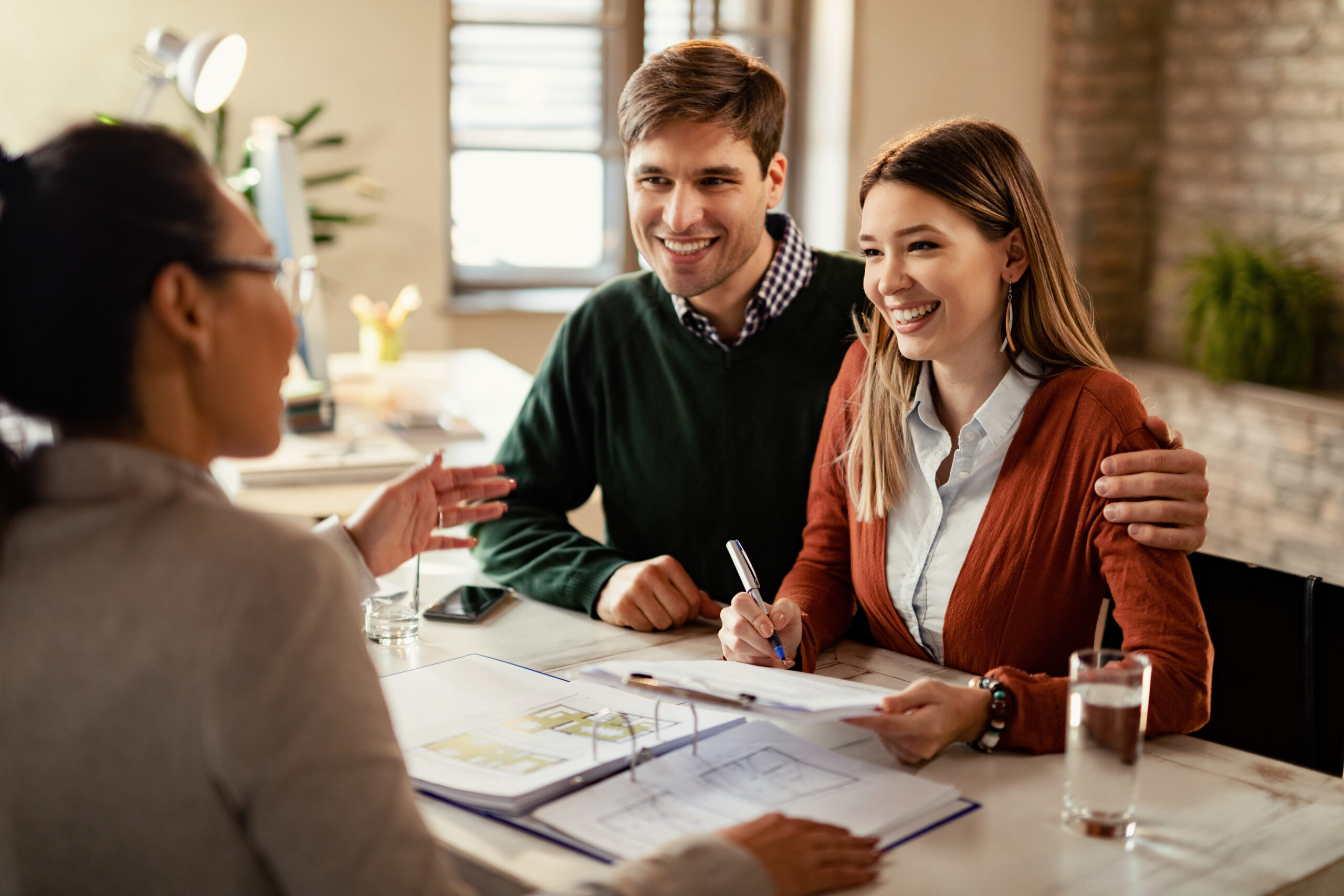 Young happy couple analyzing plans with their mortgage broker while having a meeting in the office.