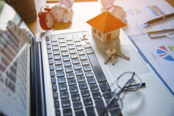 Laptop with a miniature house, keys, and business documents.