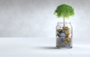 A glass jar with coins inside and a green tree growing from it symbolizing investement