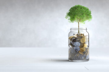 A glass jar with coins inside and a green tree growing from it symbolizing investement